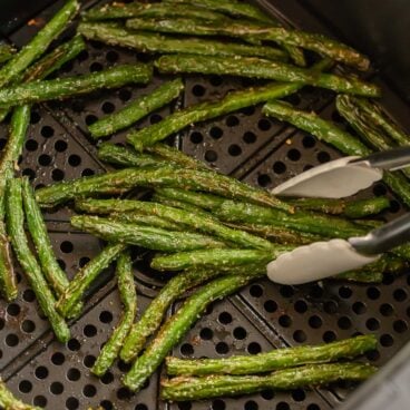 tongs picking up roasted green beans from air fryer.