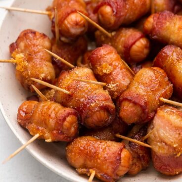 close up image of bacon wrapped smokies in white bowl.