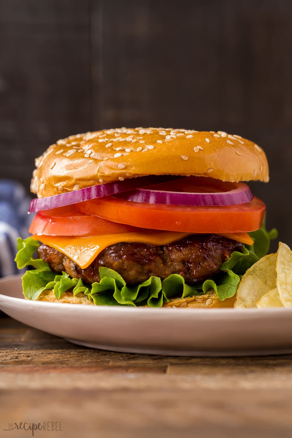 beef burger on bun with lettuce tomato and onion against black background