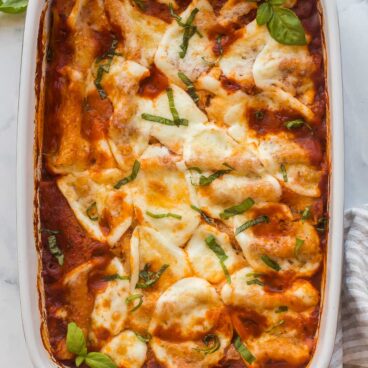 overhead image of baking dish with cheese cannelloni and fresh basil