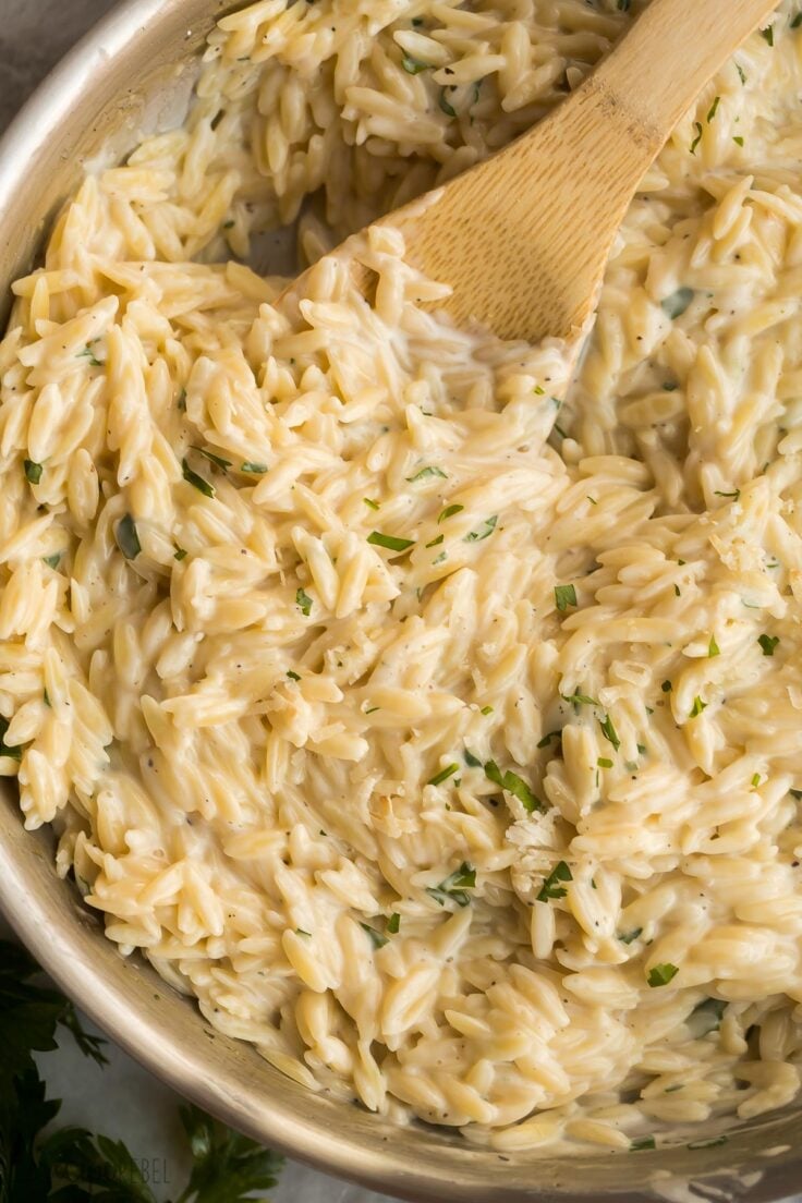 close up image of creamy orzo pasta in skillet with wooden spoon