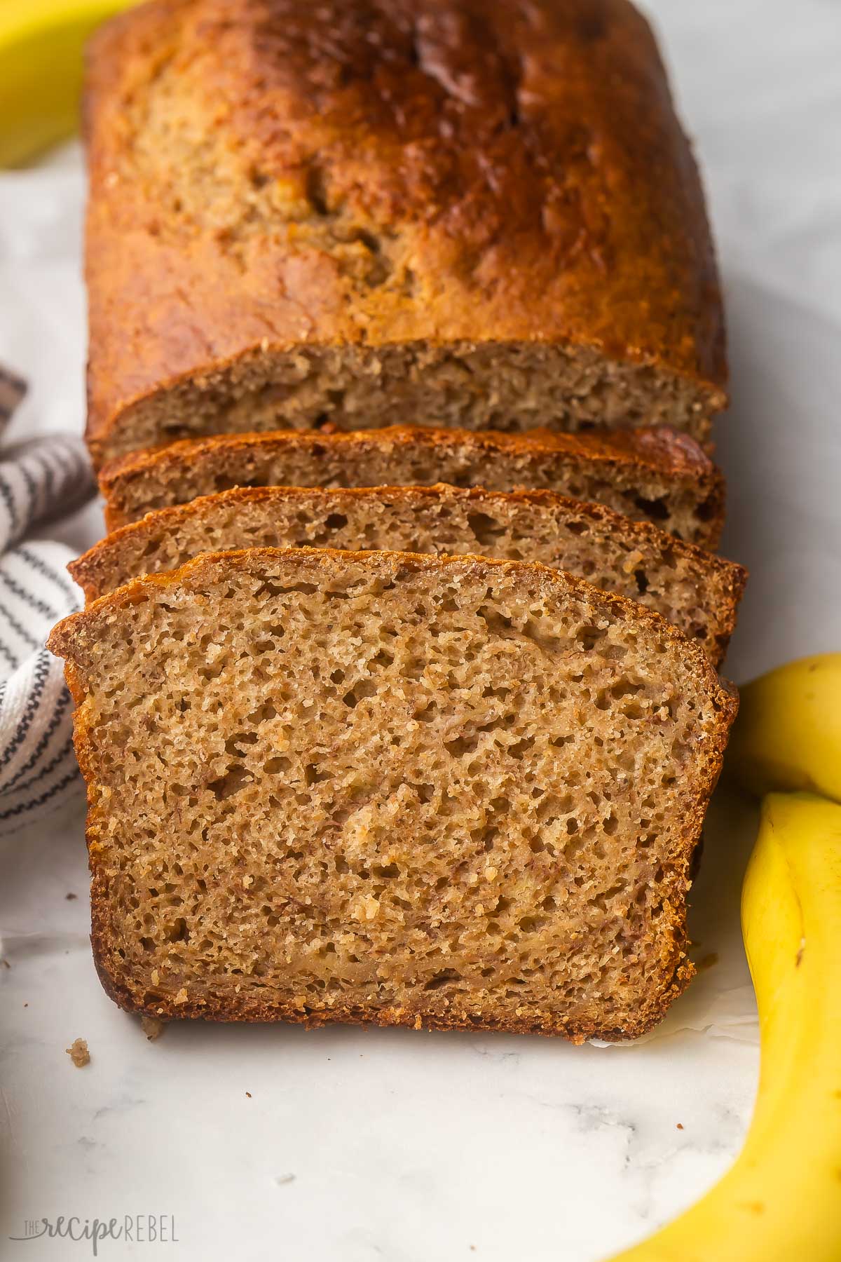 slices of banana bread leaning against loaf with banana beside.