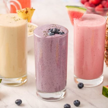 three different smoothies in glasses with a variety of fruit in the background