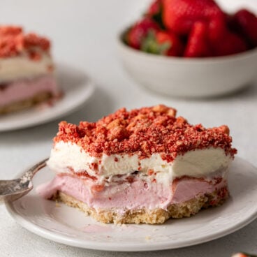 a plate with a piece strawberry shortcake ice cream bars and a bowl of strawberries in the background.